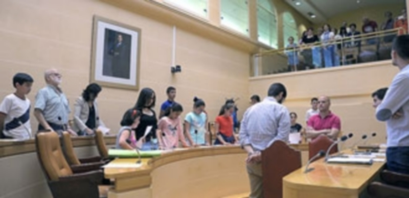 Los integrantes del pleno de la infancia escuchan respetuosamente el Himno a Segovia antes de la sesión. / KAMARERO