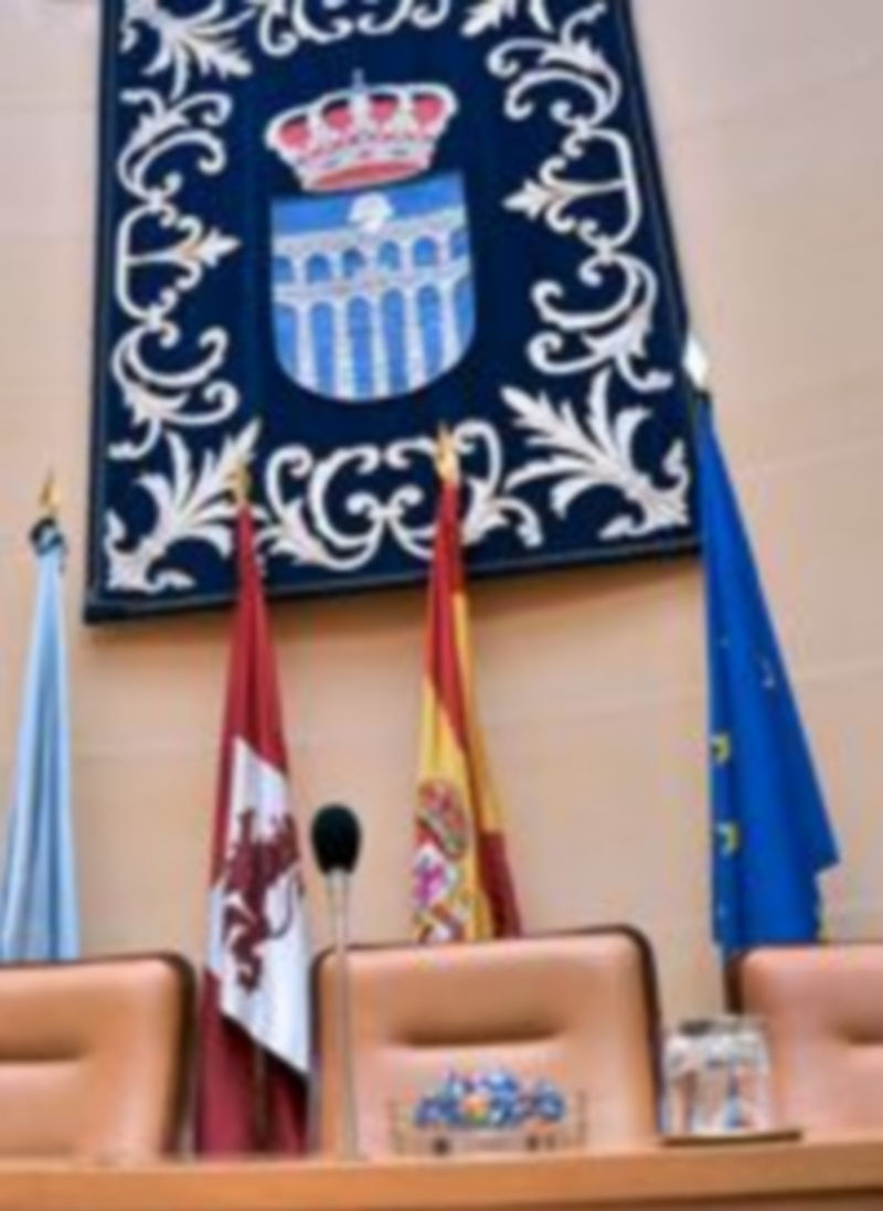 Imagen del salón de plenos del Ayuntamiento de Segovia. Un tapiz con el escudo de la ciudad engalana la mesa presidencial. / Kamarero