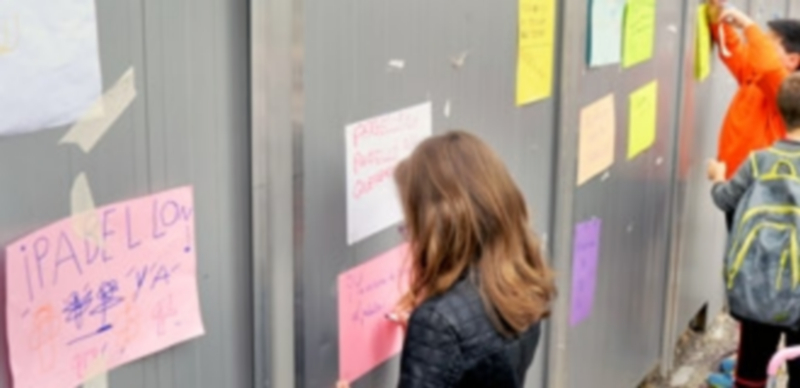 Los escolares escriben en los muros de cerramiento de las obras del pabellón su deseo de ver terminada la instalación. / K.