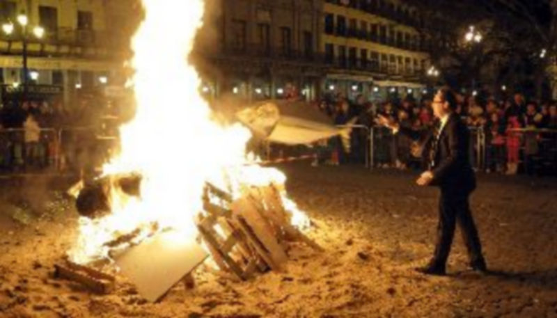El integrante de una comparsa procede a lanzar a la última sardina a la hoguera situada en la Plaza Mayor