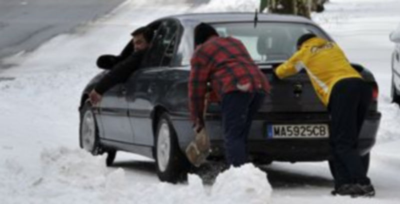 Dos  personas ayudan a un conductor a sacar su vehículo de la nieve en San Rafael./ Juan Martín