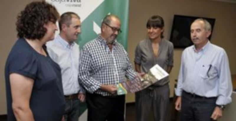 Los organizadores del evento muestran el cartel promocional de los paseos en la oficina de la Caja Rural. / Juan Martín