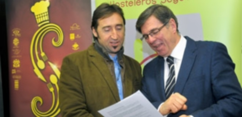 Francisco Javier García y Julián Duque comentan el programa de la semana junto al cartel anunciador del evento. / Kamarero