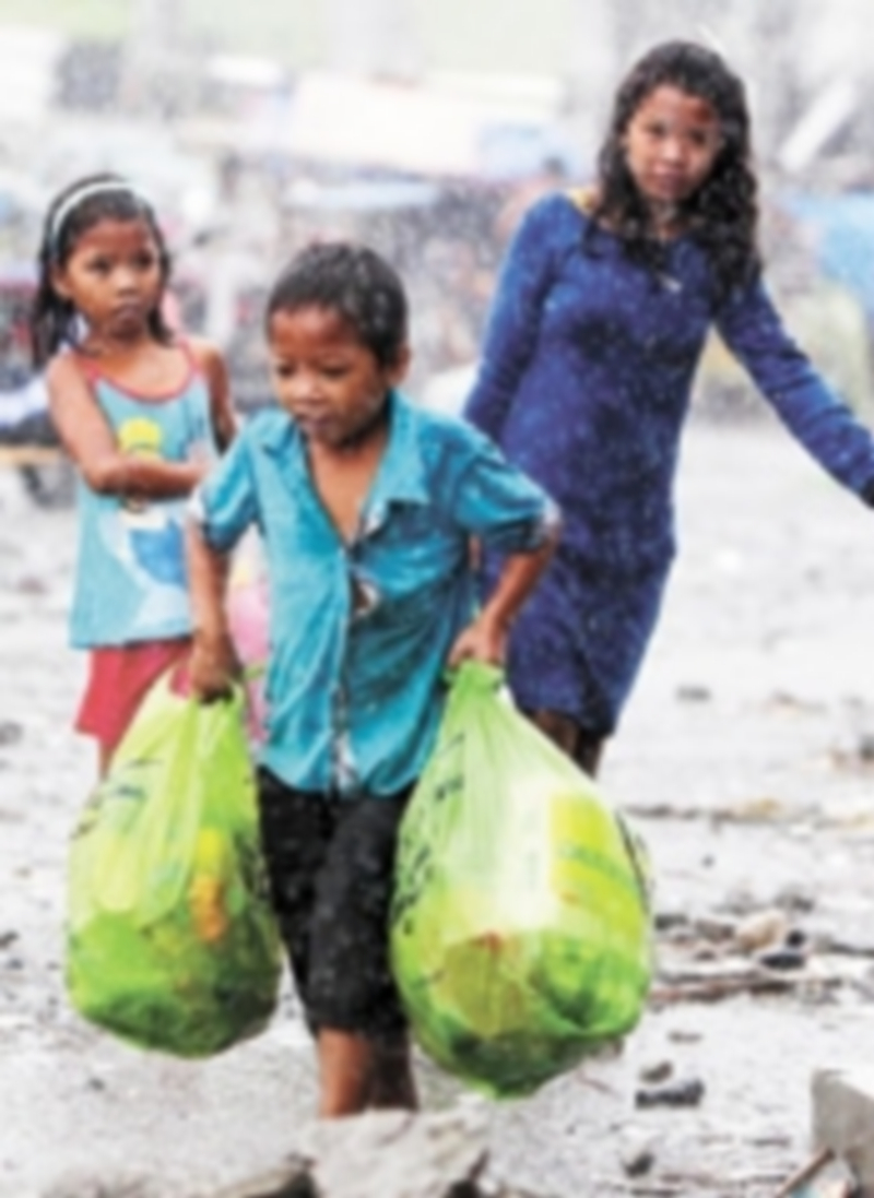 Unos niños caminan bajo la lluvia provocada por ‘Zoraida’ con provisiones entregadas por el Gobierno. / Efe