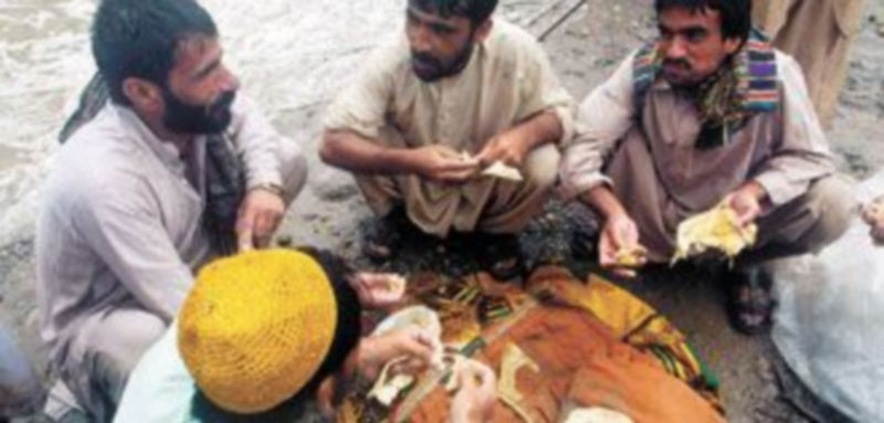 Varios hombres sacian su hambre tras recibir alimentos en una zona afectada por las inundaciones de Nowshera
