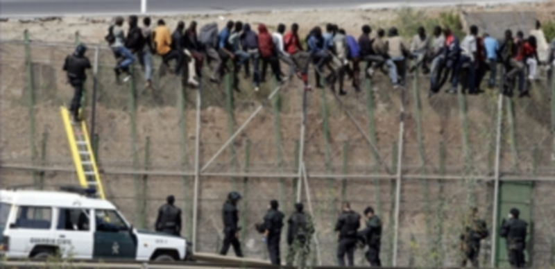 Dos de los inmigrantes encaramados a la valla de Melilla desde esta madrugada bajan de la verja y son entregados a Marruecos. / Efe