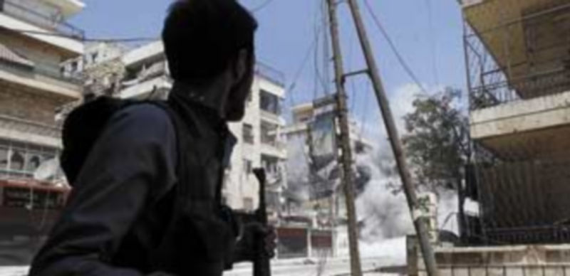 Un rebelde cruza una calle en Alepo en el instante en el que se produce una explosión en un edificio cercano. / Reuters