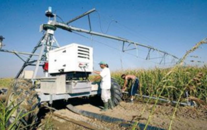 Dos agricultores controlan la instalación de un pivot de riego en una plantación de maíz.