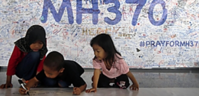 Un grupo de niños de origen malasio escriben mensajes en uno de los muros homenaje a las personas que viajaban en el avión desaparecido. / Efe
