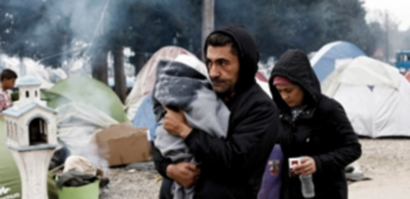 Una familia de refugiados camina con su hijo a través de un campamento en la ciudad griega de Idomeni. / Efe