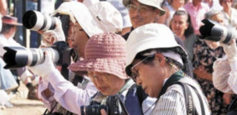 Un grupo de turistas japoneses fotografían un acto festivo celebrado en las calles de la aldea onubense de El Rocío. / Efe