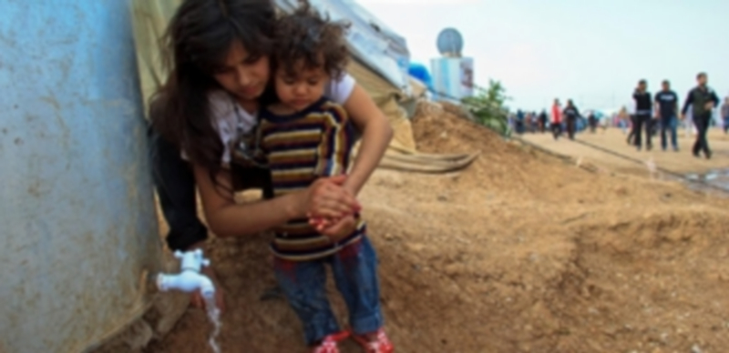 Una mujer lava a un niño pequeño en un campo de refugiados sirios en las afueras de una tienda de campaña construida con recursos escasos. / Agencias