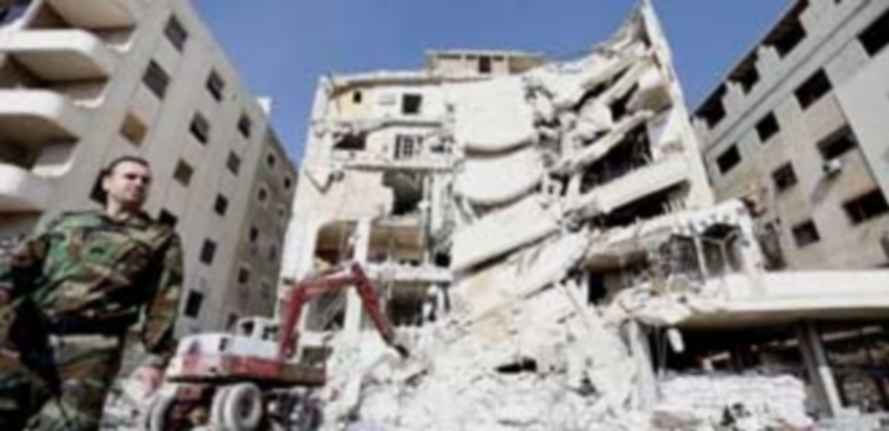 Un soldado sirio aguarda frente a las ruinas de un edificio en Damasco