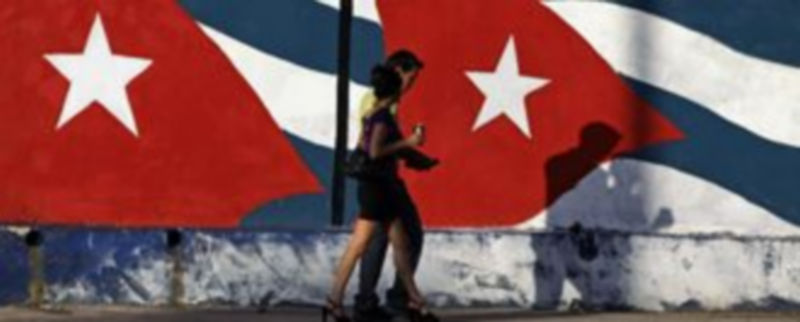Un pareja pasea por La Habana frente a un mural con la bandera de la estrella solitaria