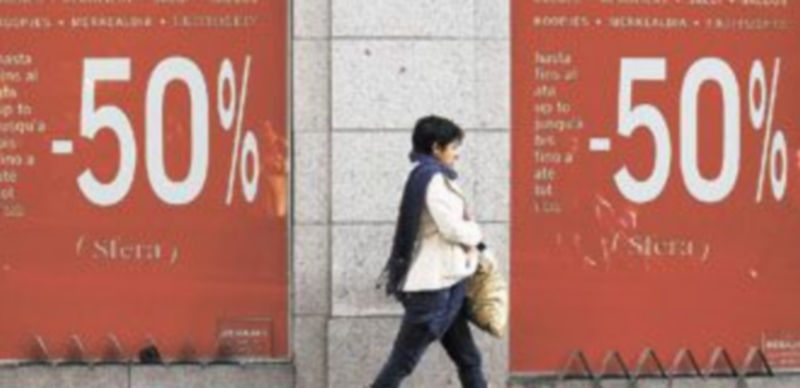 Una mujer camina frente a los escaparates decorados con grandes carteles publicitarios que anuncian los descuentos ofrecidos p0r los establecimientos. / Reuters
