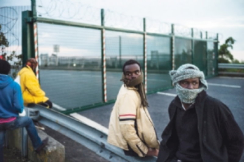 Algunos inmigrantes aguardan tras una vaya para poder tomar un tren que les lleve al Reino Unido. / EFE