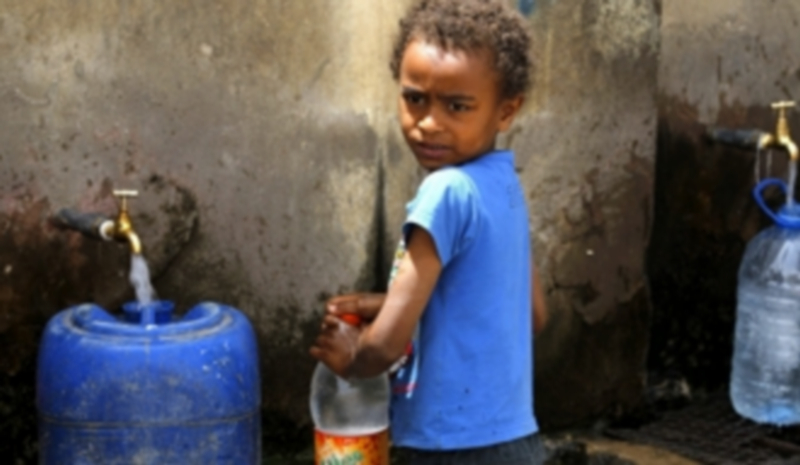 Un niño yemení llena una botella con agua potable en una fuente de Saná