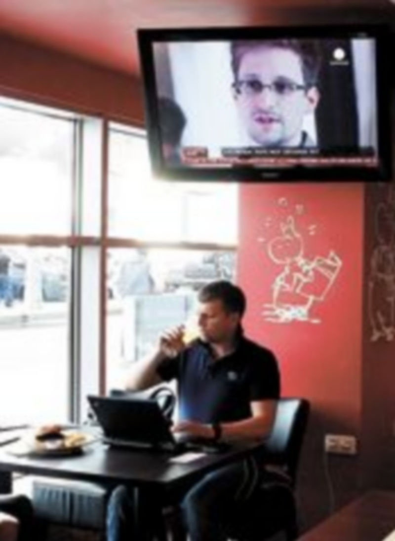 Un viajero descansa en la cafetería del aeropuerto Sheremetievo con una imagen de Snowden en la televisión. / Reuters