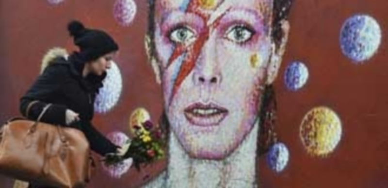 Una mujer deposita flores en el altar espontáneo que los británicos construyeron al pie del mural que homenajea a David Bowie en Reino Unido. / Efe