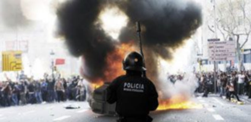 Un policía vigila el fuego de un contenedor que ha prendido un piquete para cortar una de las principales avenidas de Barcelona. /Reuters