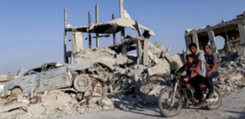 Varias personas pasan por delante de los escombros de edificios y coches en la ciudad de Kobani