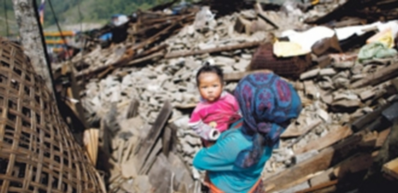 Una mujer lleva a su hija en brazos ante la imagen desoladora de los edificios hechos escombros en la ciudad de Barpak. / Efe