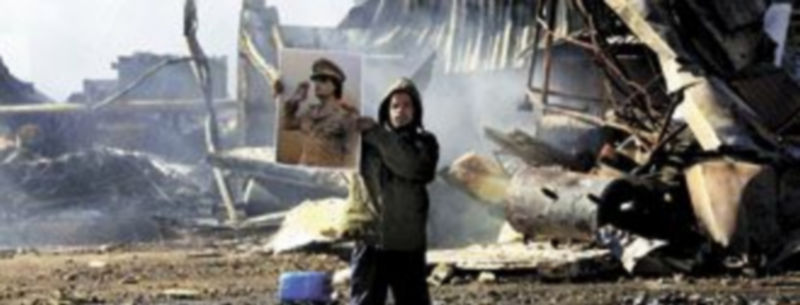 Un seguidor del líder libio muestra una imagen de Muamar el Gadafi entre los escombros de un edificio abatido en Trípoli. / Reuters
