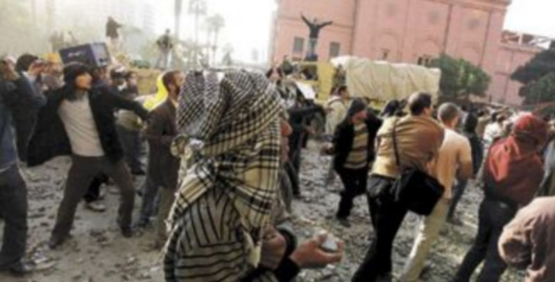 Decenas de manifestantes lanzan piedras durante los enfrentamientos entre partidarios y detractores de Mubarak; al fondo