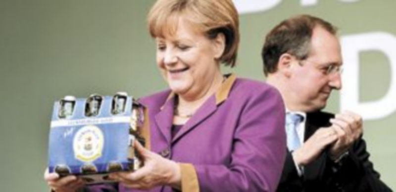 Angela Merkel recibe una caja de botellines de cerveza en un acto público organizado por una empresa germana de bebidas alcohólicas. / Reuters