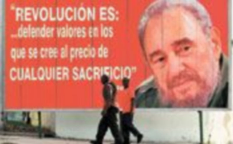 Dos cubanos caminan junto a un mural con la imagen de Fidel Castro. / Efe