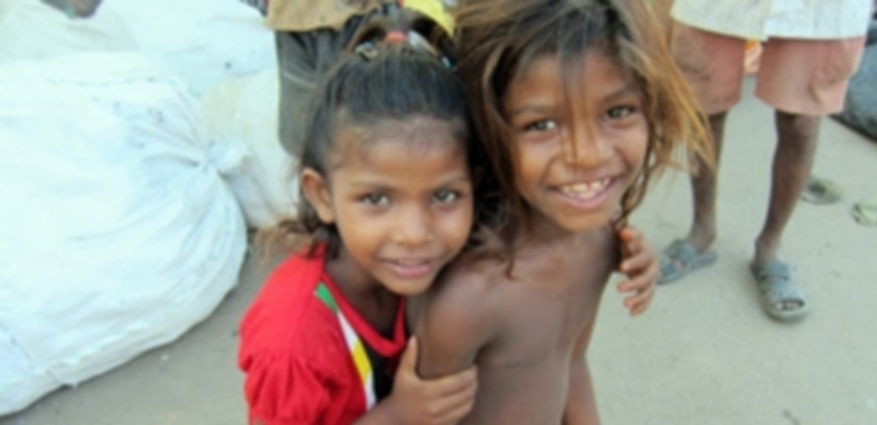 Dos niños pequeños de una barriada de una ciudad de India sonríen a la cámara pese a su estado de suma pobreza./ EP