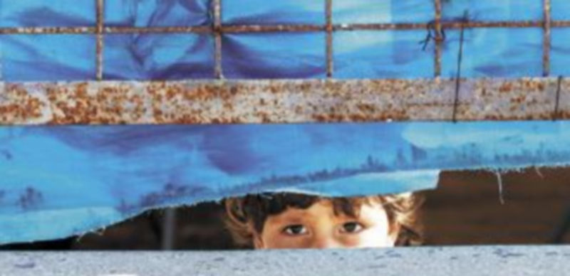 Un niño sirio observa oculto los ataques de las tropas del régimen desde un campo de refugiados en la frontera con Turquía. / Reuters