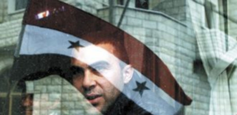 Una bandera siria se refleja en el cristal de una vivienda del barrio de Baba Amro. / Reuters.