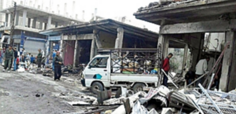 Varias personas inspeccionando el área destruida por un doble atentado perpetrado en el pueblo de Al Mujarram