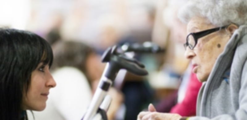 Una persona joven charla con una mujer de la tercera edad que necesita apoyo para poder moverse. / Europa Press