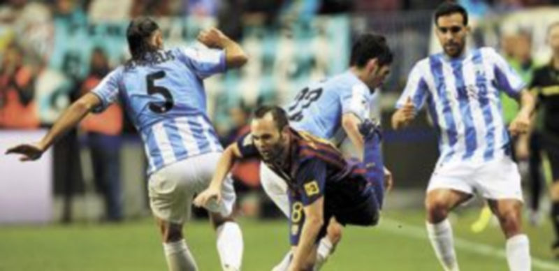 Sin margen para el tropiezo 1 Iniesta cae en una acción del encuentro de la primera vuelta ante la presión de tres jugadores malacitanos. / Reuters.