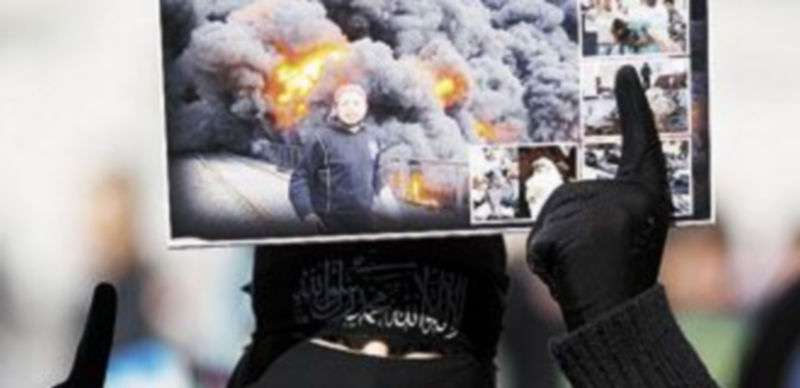 Una mujer muestra una serie de fotografías con bombardeos sobre Homs. / Reuters