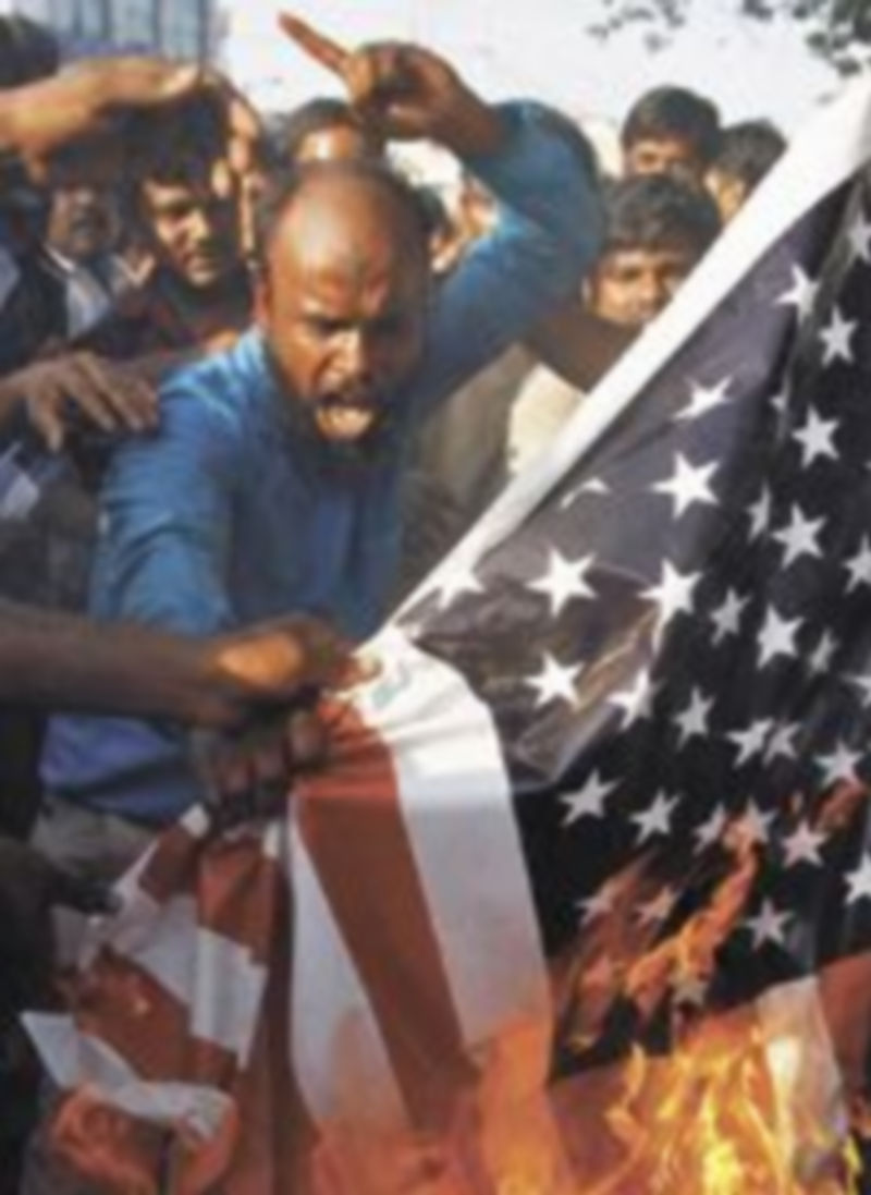 Varios asaltantes queman una bandera norteamericana. / Reuters