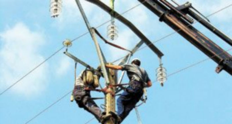 Dos operarios de la energía arreglan una torre de alta tensión.