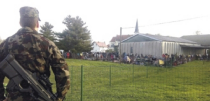 Un soldado vigila a los refugiados que se agolpan en el campamento provisional de la ciudad eslovena de Dobova. / Efe