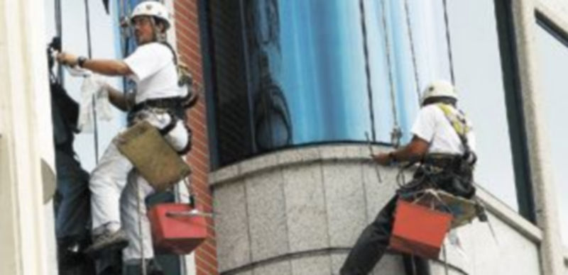 Dos trabajadores del sector de la limpieza sacan brillo a los cristales exteriores de un edificio. / Jesús Javier Matías