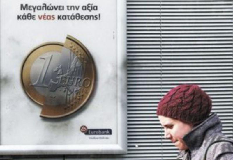 Una mujer griega pasa junto a un cartel de un banco con el símbolo de la moneda única. / John Kolesidis (Reuters)