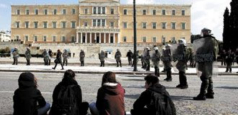 Una mujer pasa junto a la hilera de policías griegos mientras un grupo de jóvenes observan la escena frente la Parlamento en Atenas. / John Kilesidis (Reuters)