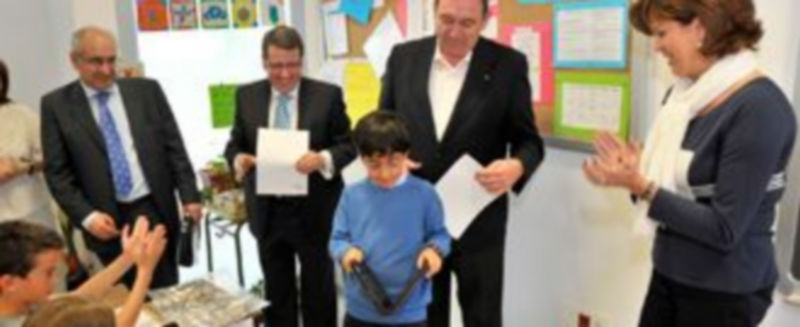 El niño galardonado observa el ordenador portátil que recibió como premio de manos del director provincial de Educación