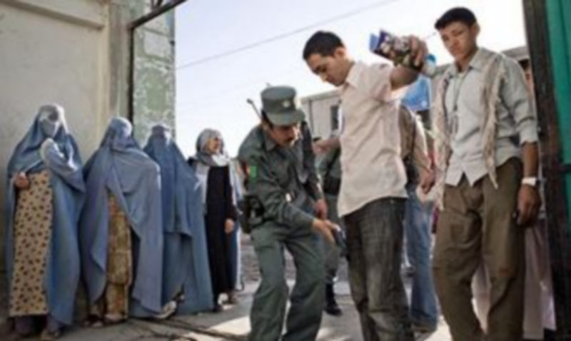 Un policía afgano requisa a los votantes en un centro electoral hoy