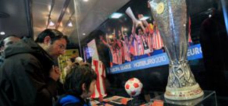 Dos visitantes observan varios de los objetos expuestos junto a la copa de la Europa League. / Kamarero