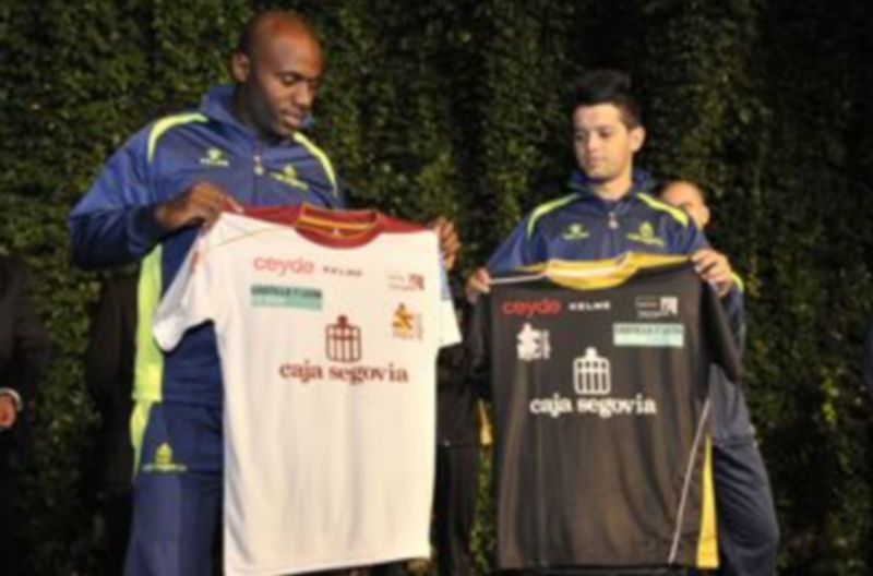 Tobe y Lin sujetan una camiseta con el logotipo de Caja Segovia en el centro de la misma como patrocinador principal del equipo. / Kamarero.