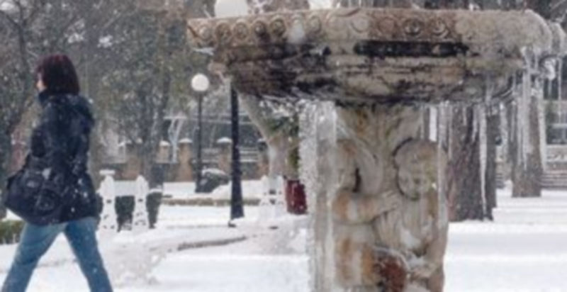 El agua de una fuente helada y una joven paseando por un parque de la ciudad de Soria con una importante capa de nieve. / Ical