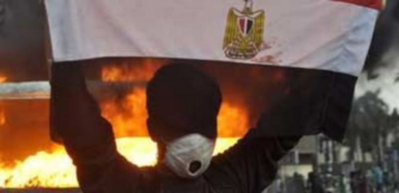 Un egipcio sujeta la bandera nacional frente a un coche de la policía que está en llamas en El Cairo. /EFE