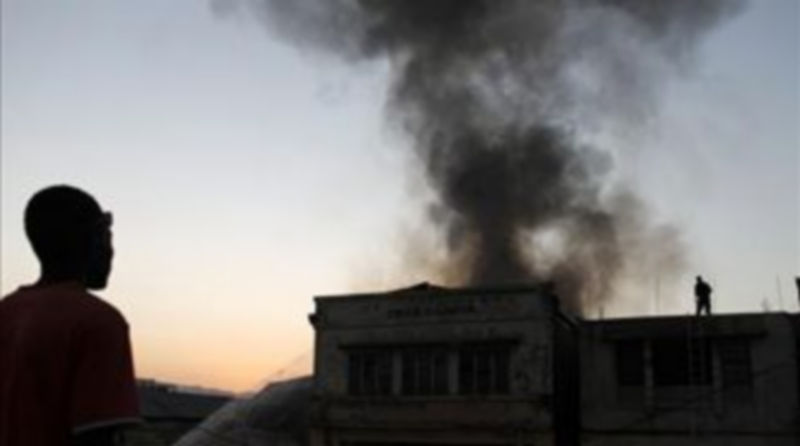 Un hombre observa mientras bomberos tratan de apagar el fuego en un local comercial./EFE